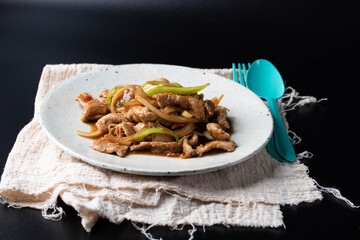 Stir-fried pork bell pepper in a white plate on a black background.