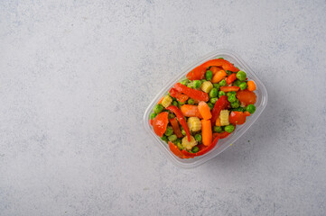 Frozen vegetables corn, red pepper, peas, carrots, tomatoes in plastic tray on an gray background top view, copy space for text