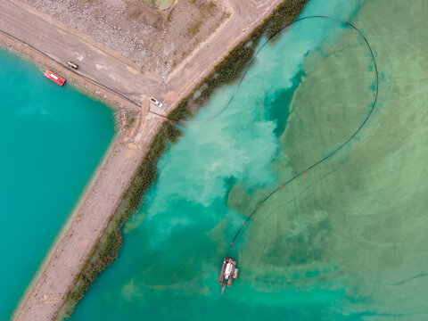 Aerial drone view of colorful turquoise blue mining tailings with vehicles and boat