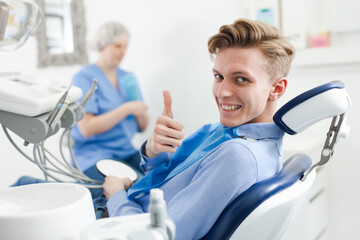 Obraz premium Portrait of satisfied man visiting dentist giving thumbs up in the dental clinic. High quality photo