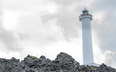 Cape Zanpa Lighthouse, Okinawa, Japan with surrounding volcanic rock formation and silver line sky with grey clouds