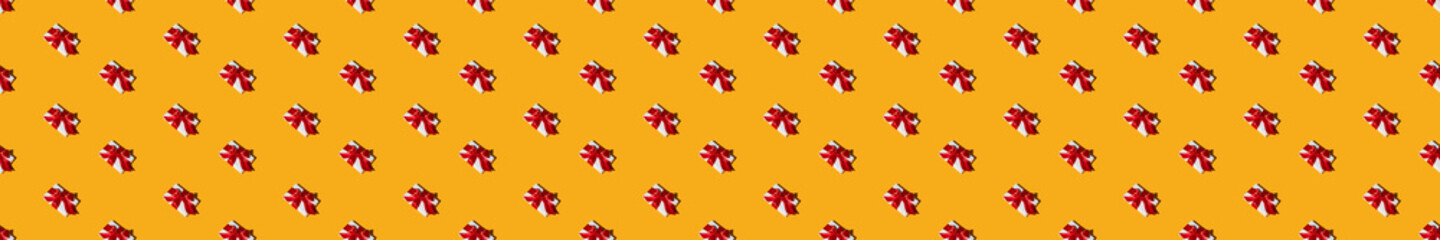 Orange festive background. Gift seamless pattern. Holiday decor. Congratulation greeting design. Minimalist symmetrical composition of white boxes with red ribbon bows isolated on bright yellow.