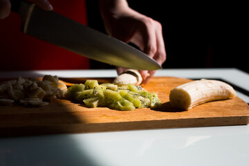 Woman's hands cutting fresh banana on the wooden board on the kitchen