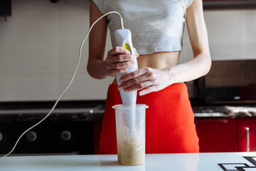Woman with hand blender making sweet banana protein milkshake. sport nutrition diet after gym. Healthy lifestyle