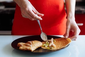 Woman's hand decorates pancakes with a fruits kiwi and banana. Black plate, white table