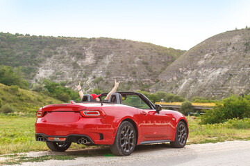 young man in red cabriolet coupe car on the traveling in mountains