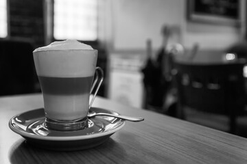 A transparent glass of cappuccino with foam on a table in a cafe. Black and white photo.