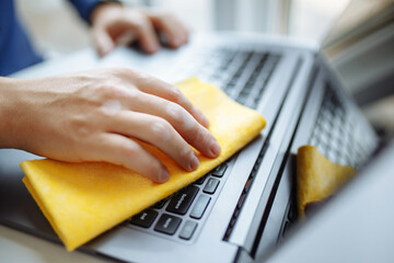 Closeup of the man's hands cleaning laptop's keyboard with a yellow rag and sanitizer to prevent coronavirus spread during global pandemic quarantine. Health care and removing bacteria from gadgets.