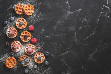 Obraz na płótnie Canvas Traditional Belgian waffles with fresh berries on a black stone background. Top view, flat lay, copy space, toned