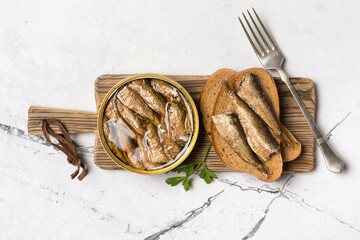 A can with golden sprats in oil and fish sandwiches on wooden board