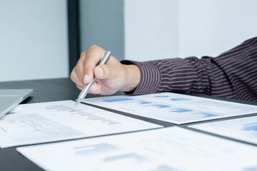 The hands of a male businessman are analyzing and calculating the annual income and expenses in a financial graph that shows results To summarize balances overall in office