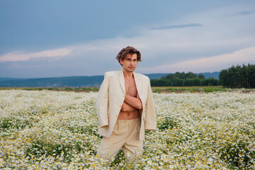 Naklejka na ściany i meble Tall handsome man standing in camomile flowers field
