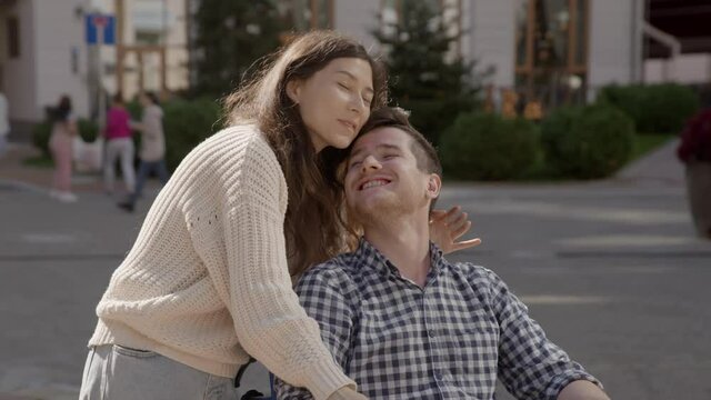 Portrait of disabled happy young man n wheelchair and his wife or friend looking at camera. Caucasian handicapped guy with paralysis living full life. Couple in love. 6k downscale 10 bit color.