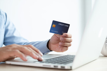The businessman's hand is holding a credit card and using a laptop for online shopping and internet payment in the office