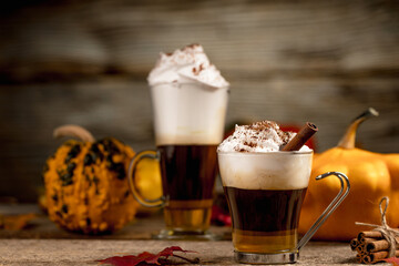 Pumpkin spice latte with cinamon powder and delicious flavours on the old textured wood table with colorful dry leaves and pumpkins