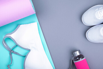 Top view of white sport shoes sneakers blue pink yoga mat, sport bra top, glass water bottle on pastel grey background. Yoga pilates or fitness practice. Losing weight and sport concept. Flat Lay.