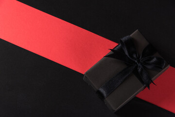 Black Friday sale shopping and Boxing Day concept, Gift box wrapped black paper and black bow ribbon present, studio shot isolated on red and dark background