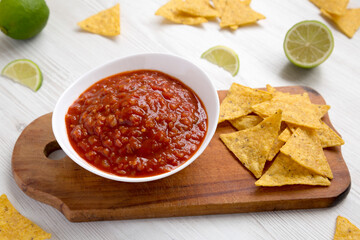 Homemade Tomato Salsa and Nachos on a rustic wooden board on a white wooden background, side view.