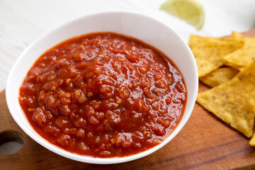Homemade Tomato Salsa and Nachos on a rustic wooden board on a white wooden background, side view. Close-up.