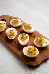 Homemade Deviled Eggs with Chives on a rustic wooden board on a white wooden background, side view. Copy space.