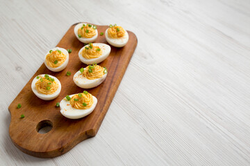 Homemade Deviled Eggs with Chives on a rustic wooden board on a white wooden background, low angle view. Copy space.