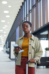 Portrait of African young woman standing with luggage and holding airplane tickets she looking at camera at the airport