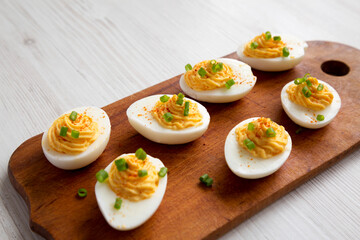 Homemade Deviled Eggs with Chives on a rustic wooden board on a white wooden background, low angle...