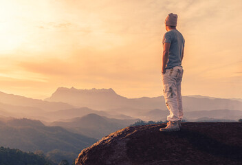 Young man standing on rock while admiring view in mountains at sunset