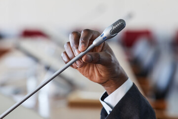 Close-up of businessman holding microphone and speaking in it during conference
