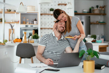 Young woman suprise her husband with cookie. Happy couple enjoying at home.
