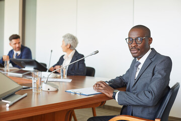 Portrait of African leader looking at camera while sitting at the table with business people at board room