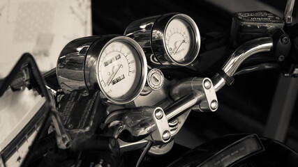 Pointer chrome speedometer and tachometer with keyhole on the handlebars of a motorcycle close-up in  garage. Monochrome dashboard of an old-style sports motorcycle, side view. Black and white photo