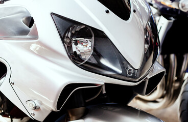 Obraz na płótnie Canvas Pair headlights front side view of motorcycle in showroom close up. Glossy white windproof shield with lamp and air intake of sportbike. Front part of modern motorcycle in salon, with steering wheel