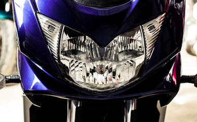Big headlight front view of motorcycle in showroom with soft-focus, close up. Glossy purple...