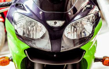 Pair headlights front view of motorcycle in showroom close up. Glossy green-black windproof shield...