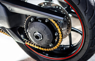 Fototapeta na wymiar Rear wheel of a sports motorcycle with red-black cast disc, close-up. Running gear, chain, sprocket, motorcycle tire, brake discs. Road fast motorcycle in the garage for repair, maintenance.