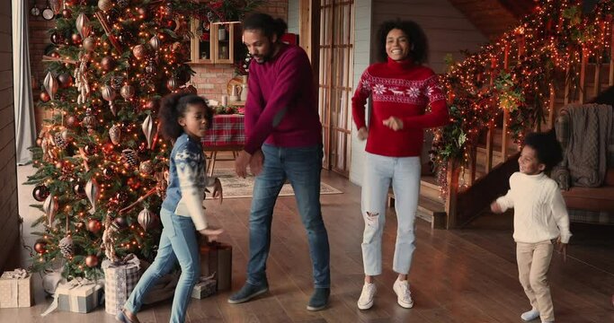 Full african family couple and kids gathered in living room decorated with twinkled lights glowing Christmas tree listen funky music dancing enjoy winter holidays. New Year celebration, hobby concept