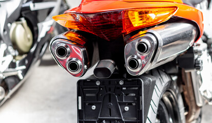 Exhaust pipes and brake light of orange motorcycle closeup. The noise of sports bike in garage. Rear view, wheel of classic road bike. Pair of chrome pipes selective focus. Place under license plate