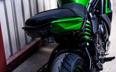 The back of a sports bike, wheel, seat, shock absorber, brake light. Fragment of a green, beautiful motorcycle, close-up, rear view. Sale of a motorcycle in a showroom in a store.