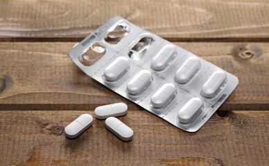 White pills in aluminum strip, tablets, medical capsules on wooden plank table background and texture