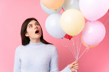 Young Ukrainian teenager girl holding lots of balloons over isolated pink background