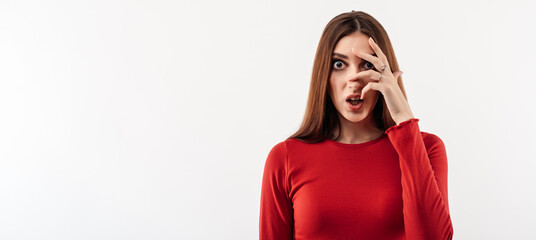 Portrait of frightened woman with long chestnut hair in casual red sweater covering her eyes with hands. Copy space