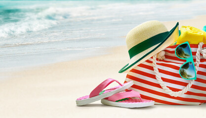 Fototapeta na wymiar Summer beach bag and accessories - sun hat, flip flops and sunglasses on sandy beach.