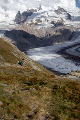 Man sitting on a hill looking at the valley glacier, Gorner, on a summer day in Switzerland. 