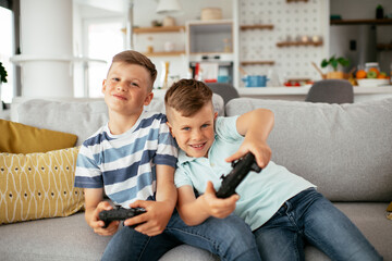 Happy brothers playing video games. Young brothers having fun while playing video games in living...