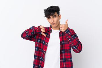 Young Argentinian man over isolated white background making good-bad sign. Undecided between yes or not