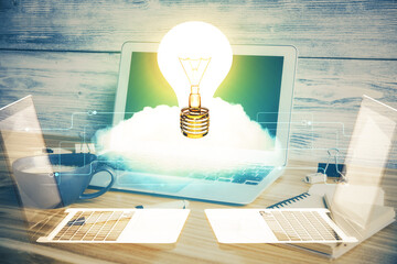 Computer on desktop in office with bulb icon hologram. Double exposure. Concept of idea.