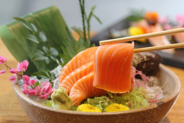 Hand holding salmon sashimi using chopsticks - Raw fresh salmon sliced served on ice with wasabi, Japanese food style. - Powered by Adobe