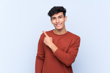 Young Argentinian man over isolated blue background pointing to the side to present a product