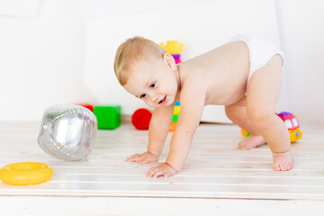 a small child a boy six months old tries to get back on his feet in a light white nursery in diapers among toys